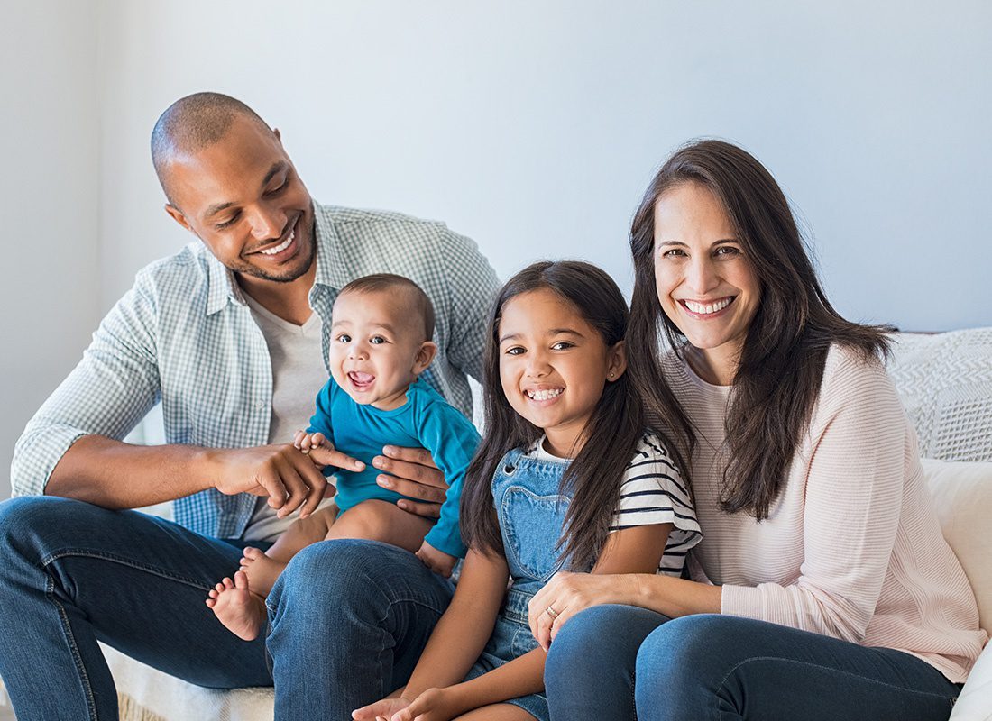 Personal Insurance - Happy Mother and Father Sit With Their Young Daughter and Baby Boy on a Sofa at Home